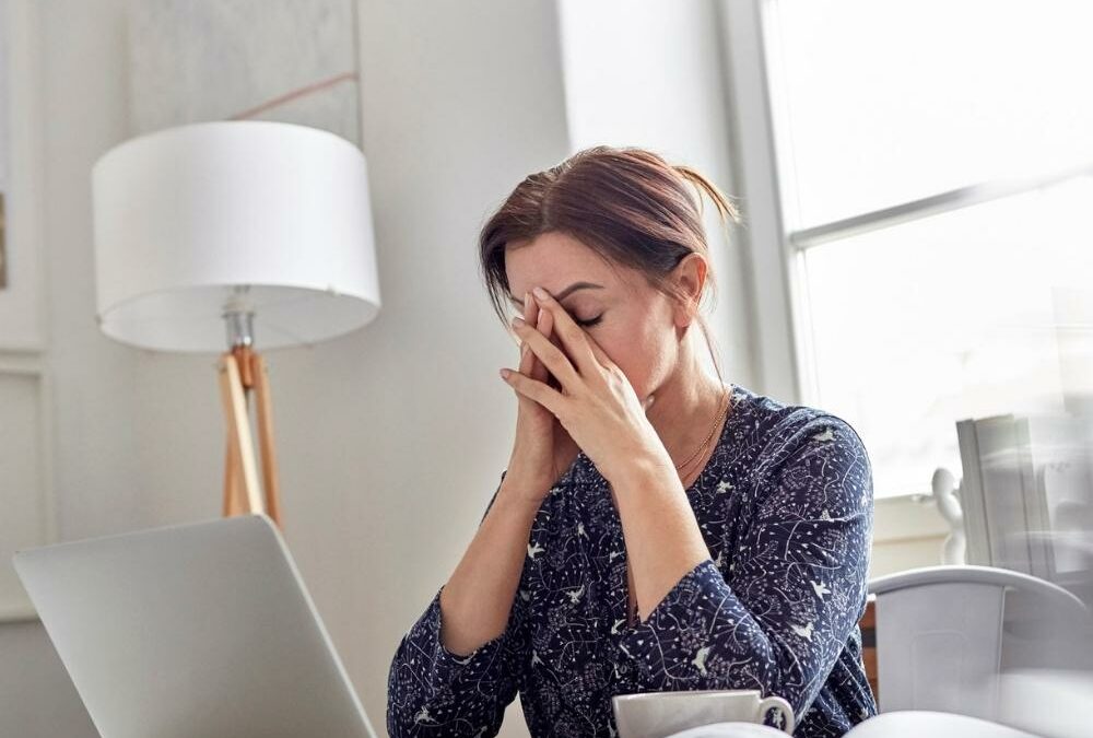 woman hiding her face in her hands while in front of a computer